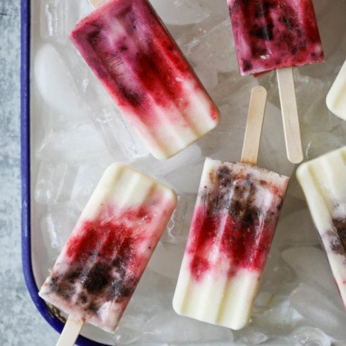 Creamy Greek yogurt popsicles with berry swirls laying on ice cubes in a metal tray