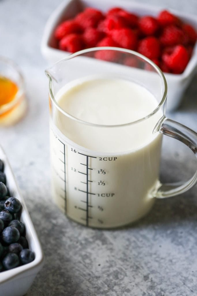 A measuring up filled with creamy kefir as part of the ingredients for creamy berry popsicles