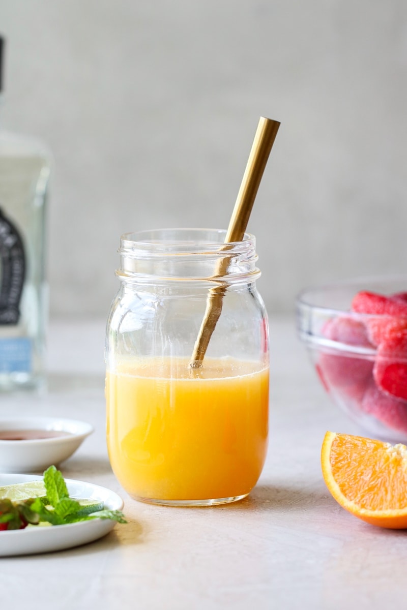 Fresh lime and orange juice in a mason jar with a gold spoon stirring it.