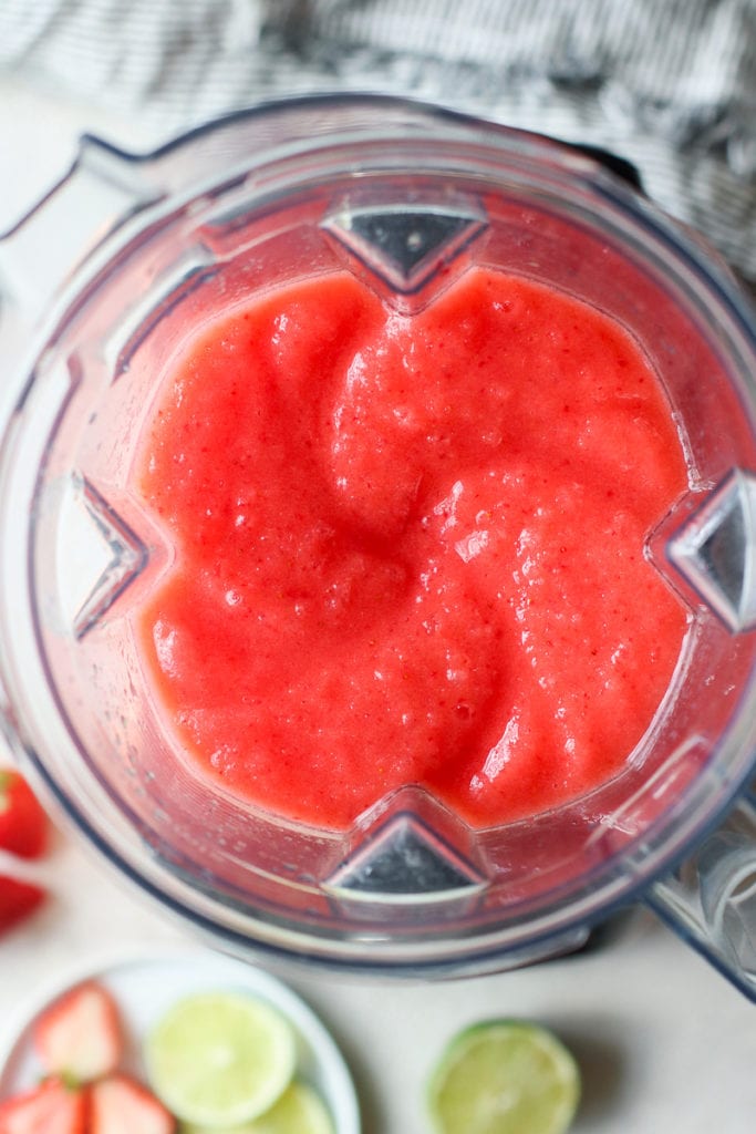 Overhead view of bright coral colored frozen strawberry margarita in a blender, freshly blended.