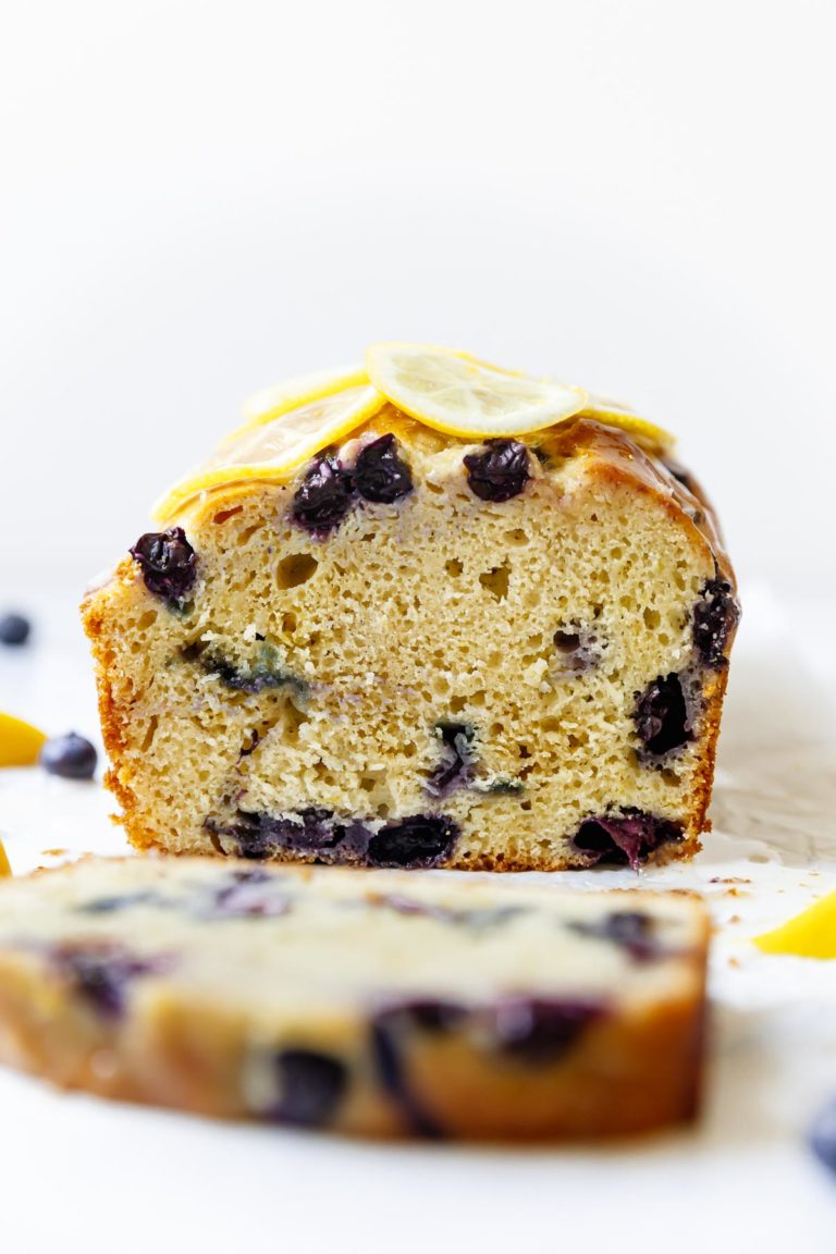 Side view of cut into lemon blueberry bread topped with lemon slices and glaze