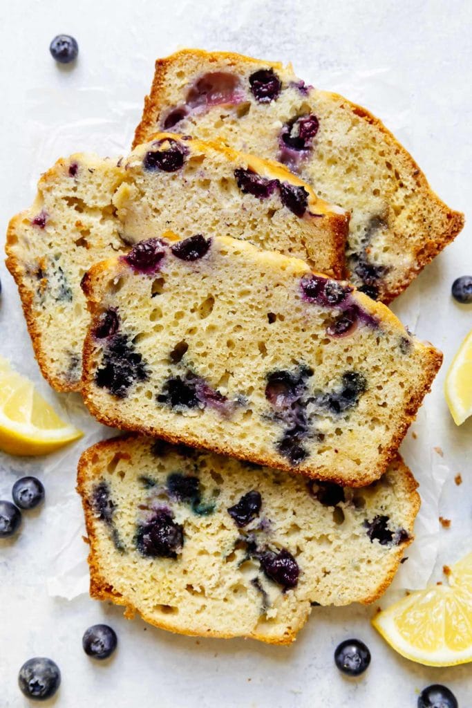 Lemon blueberry bread with glaze cut into thick slices on white background.