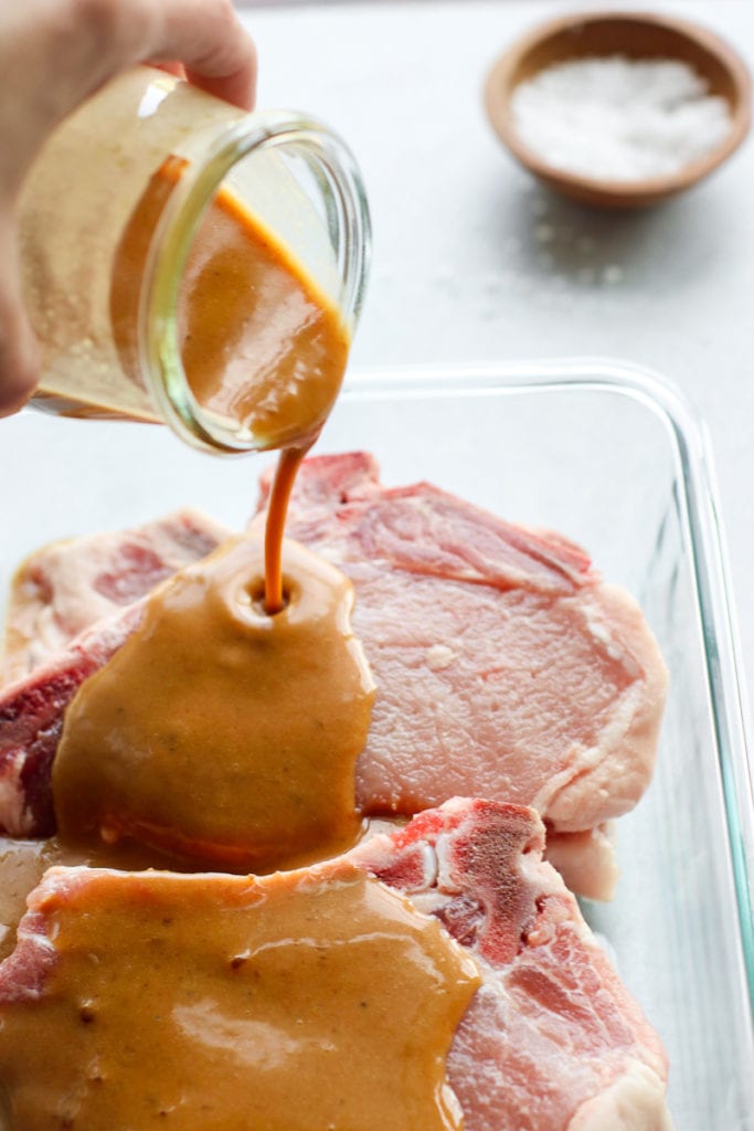 Mustard marinade being poured over pork chops in a small baking dish