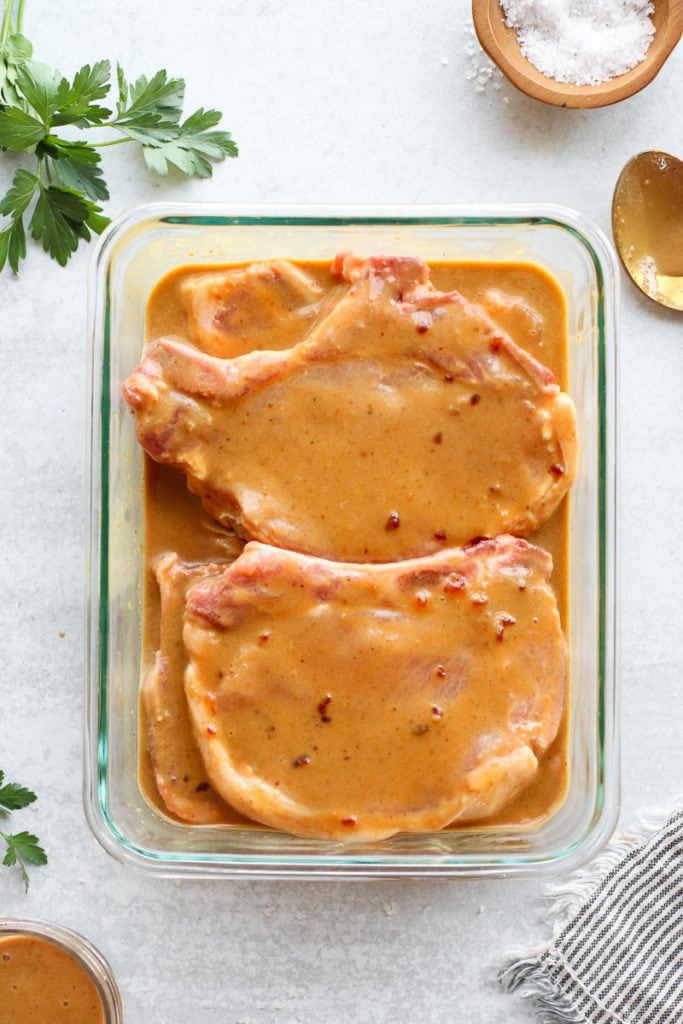 Two pork chops marinating in a small baking dish