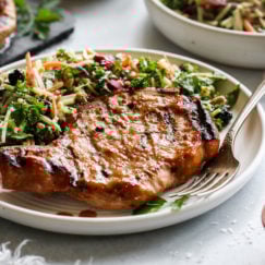 A juicy grilled pork chop marinated in homemade honey mustard marinade plated next to a side of coleslaw