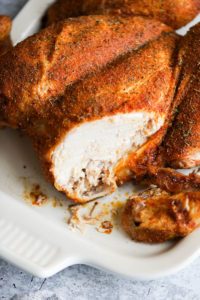 A smoked spatchcock chicken on a white platter with a slice out of the breast to show tenderness.