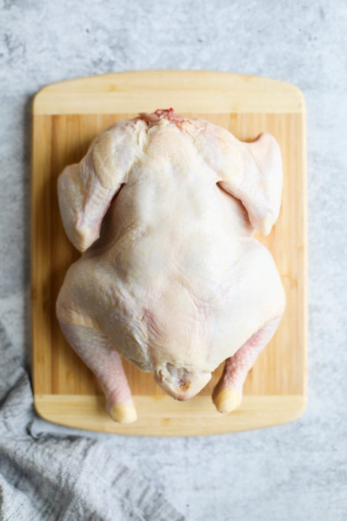 A raw whole chicken placed breast-side down on a wooden cutting board