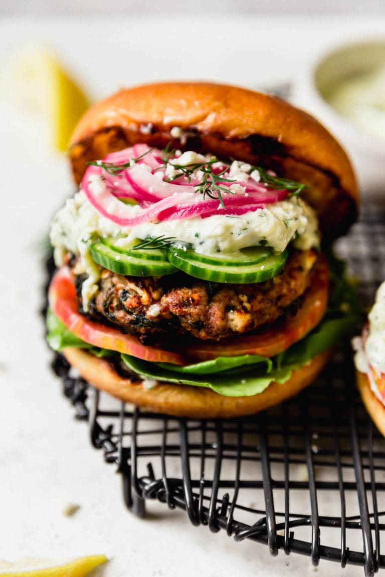 Close up view of a freshly grilled feta spinach turkey burger topped with pickled onions and a toasted bun. 