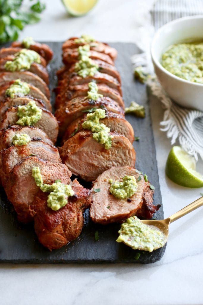 Grilled pork tenderloin cut into thick slices with green avocado-cilantro dressing on top of each slice. 