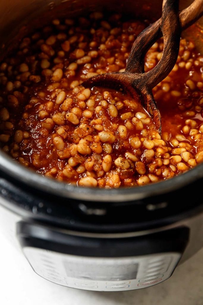 Baked beans with bacon being stirred with a wooden spoon in an Instant Pot. 