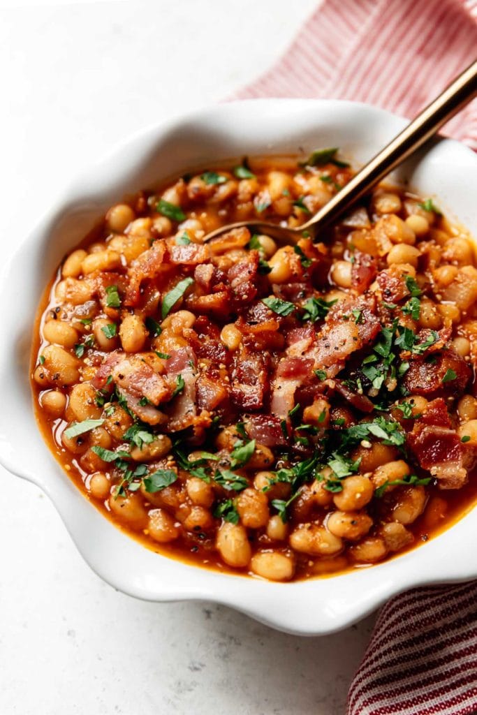 Instant Pot Baked Beans in a white bowl topped with bacon and fresh herbs. 