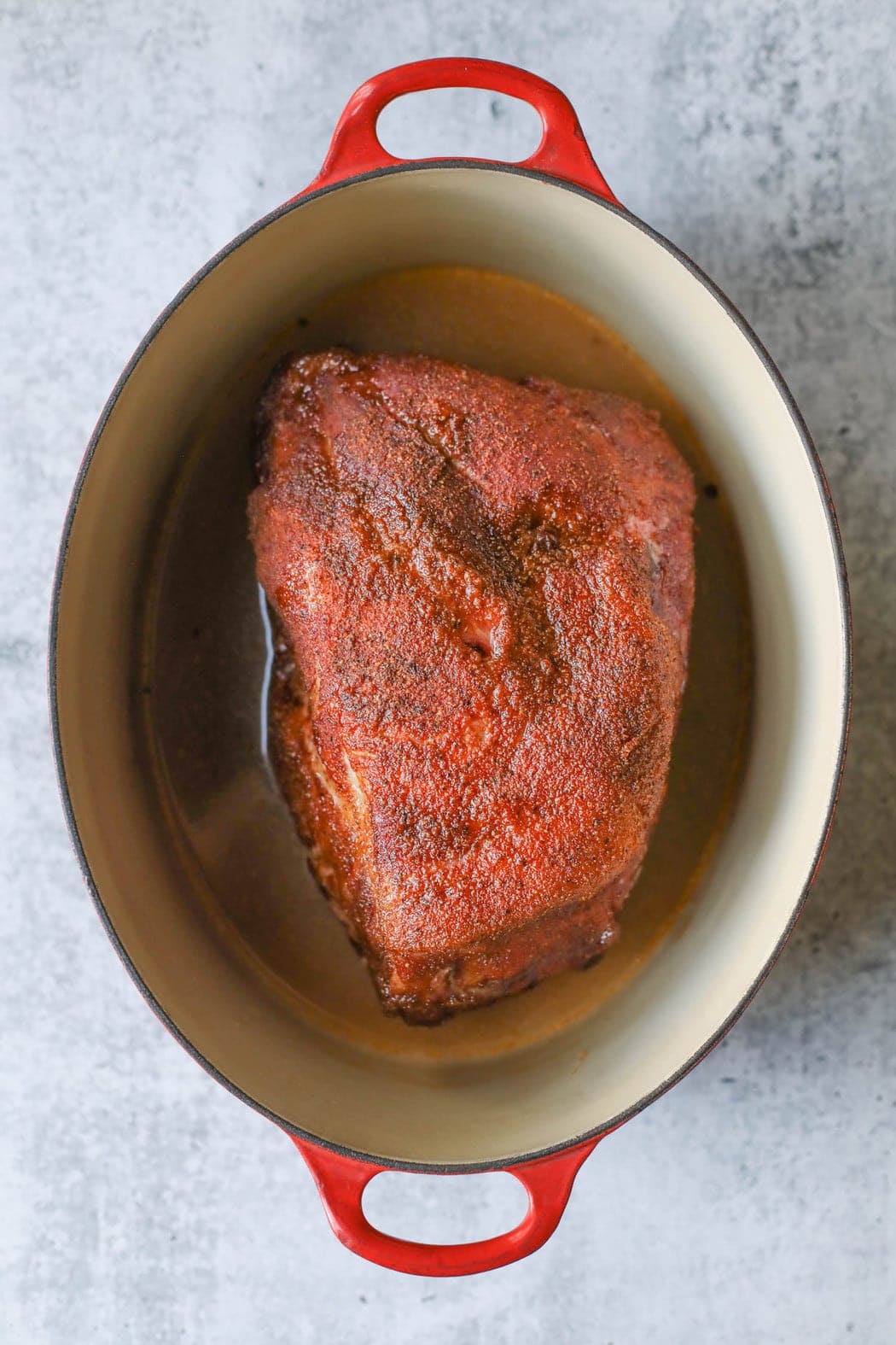 Smoked pork butt in a dutch oven soaking in liquids