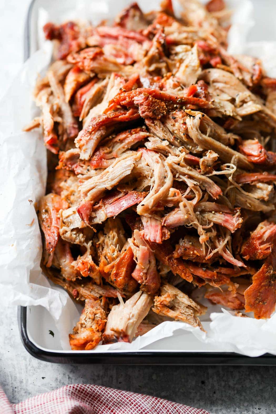 Smoked Pork Butt shredded in a white metal serving tray with a black rim and lined with white parchment