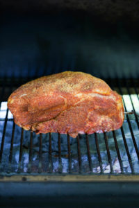 A raw pork butt heavily seasoned freshly placed on the grill ready for cooking