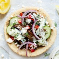 A Greek flavored vegetarian gyro on parchment paper topped with feta crumbles and tzatziki sauce