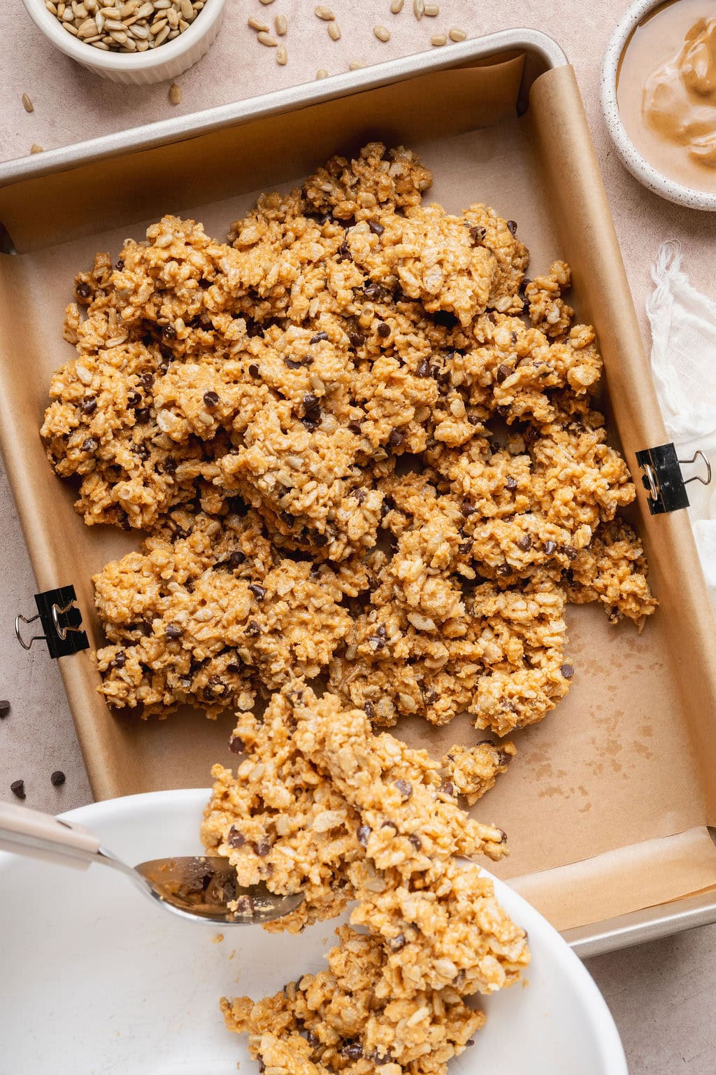A spoon scooping homemade Clif bar batter onto a parchment paper-lined baking sheet.