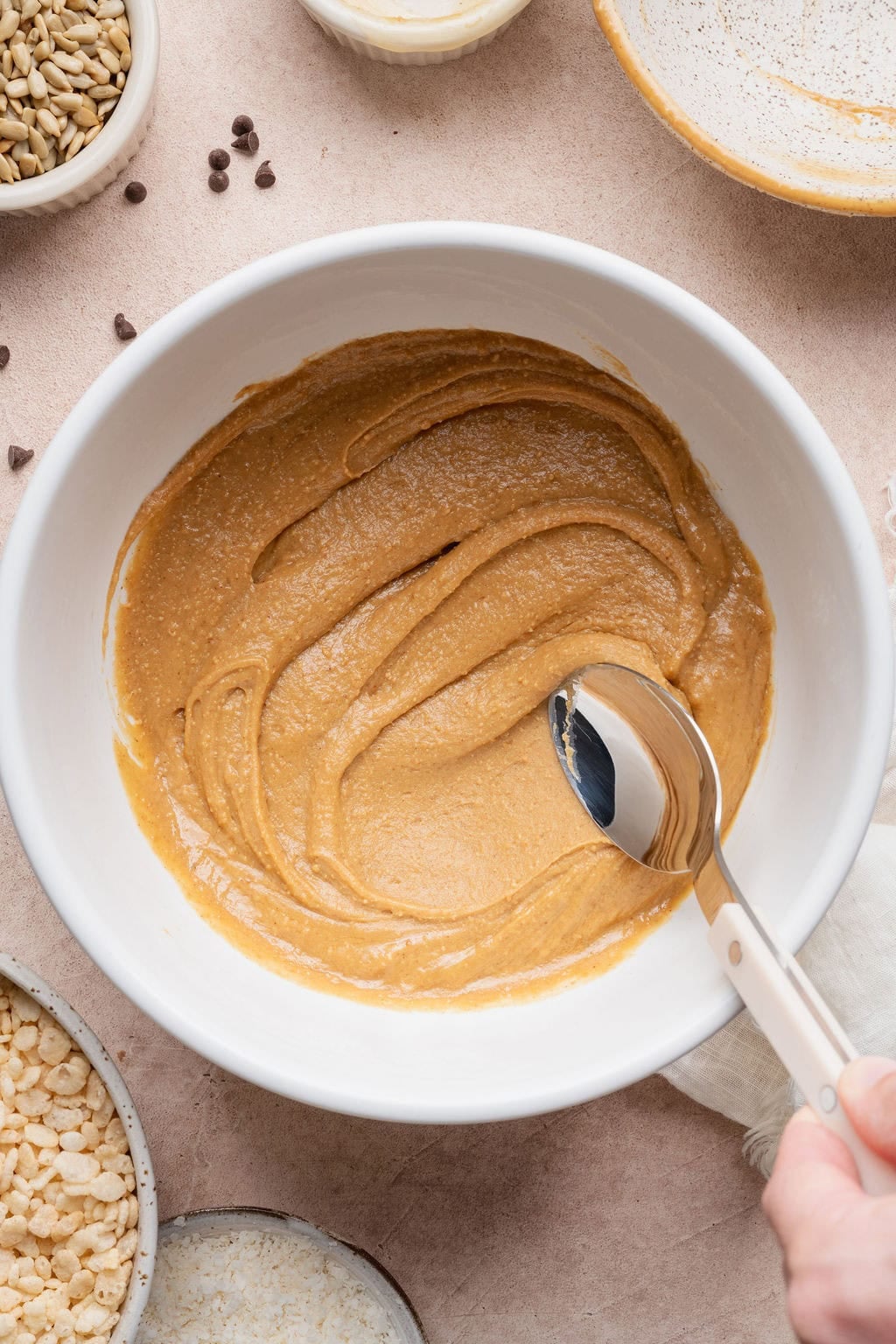 A spoon stirring peanut butter in a bowl.