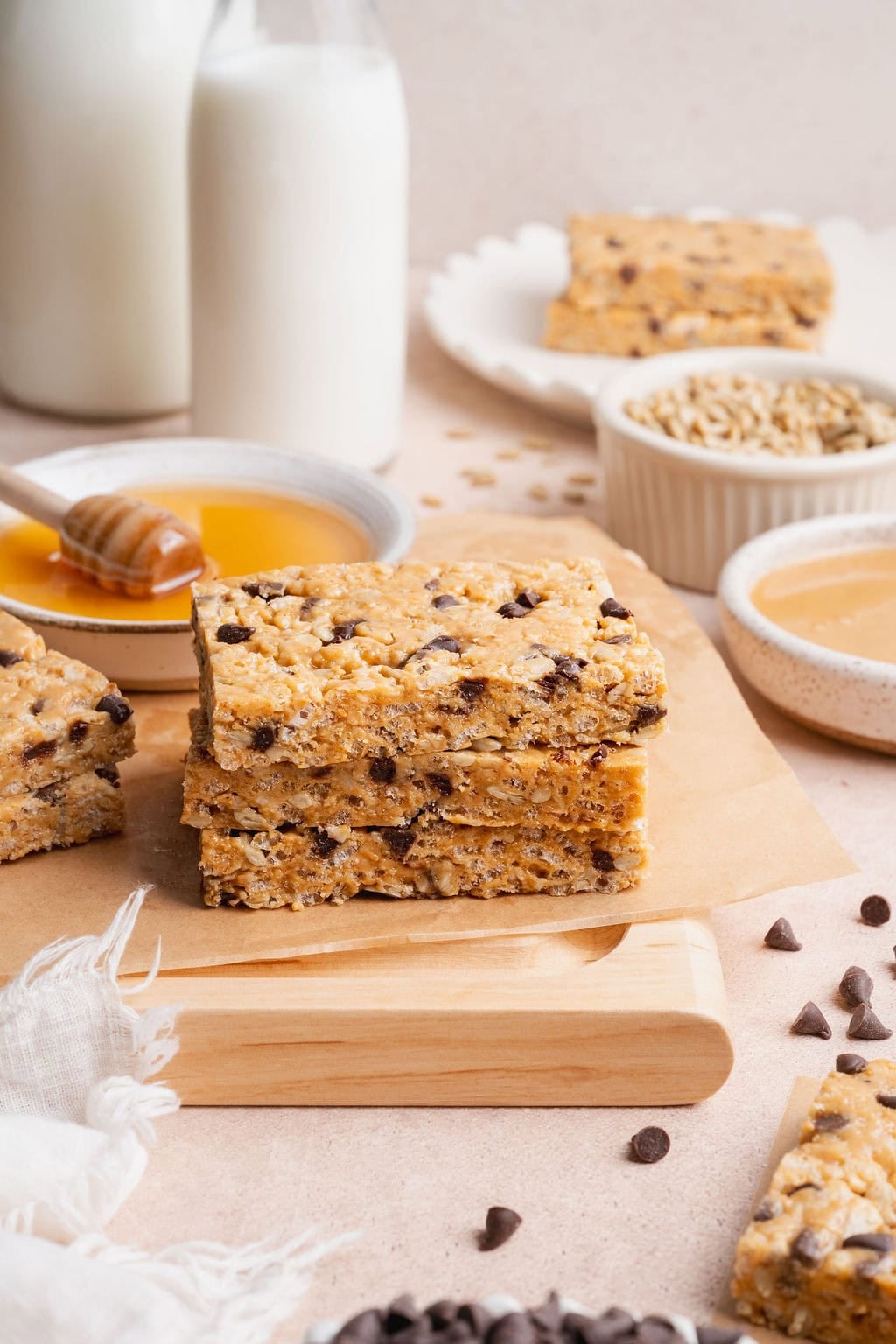 A stack of homemade Clif bars on a sheet of parchment paper, ingredients and more bars in the background.