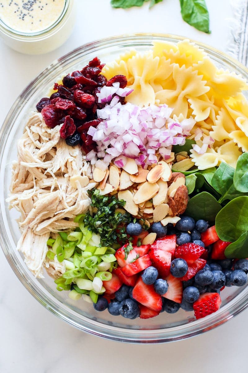Ingredient for Summer Pasta Salad with Chicken and Berries in a large, glass mixing bowl.