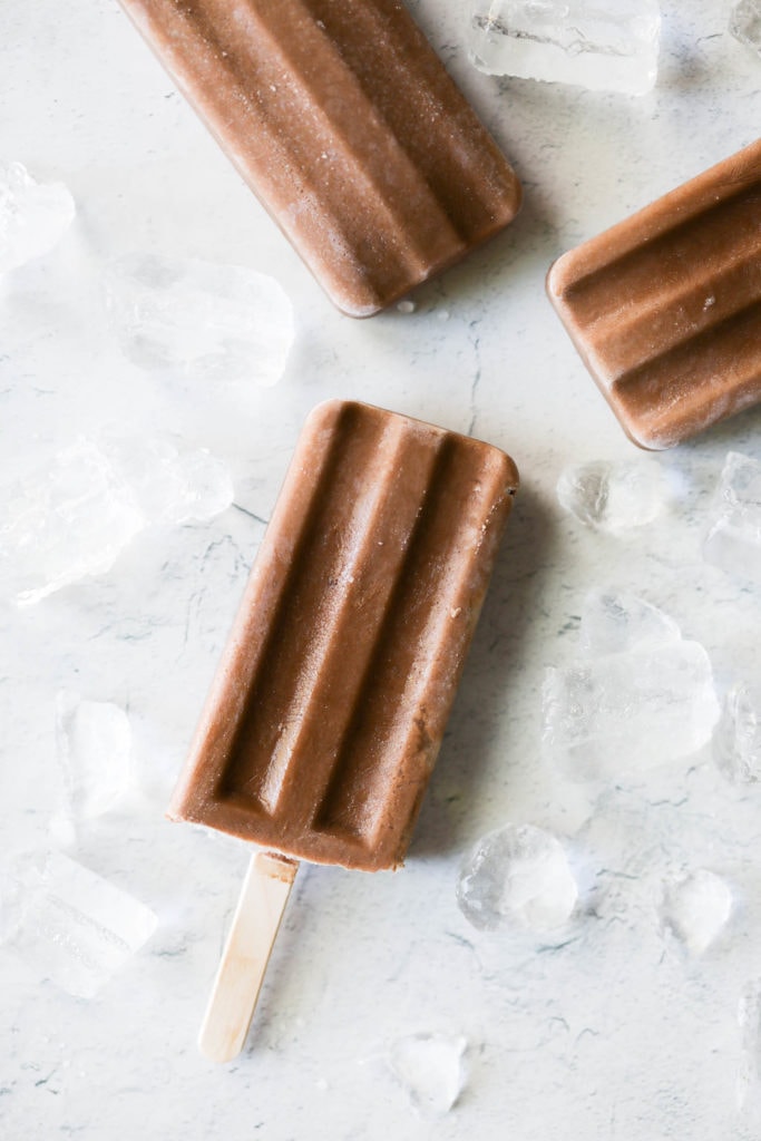 Three Dairy Free Fudgesicles laying on a counter next to ice cubes 
