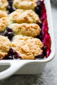 Gluten-free homemade biscuits baked over juicy and vibrant purple blueberries in a white baking dish