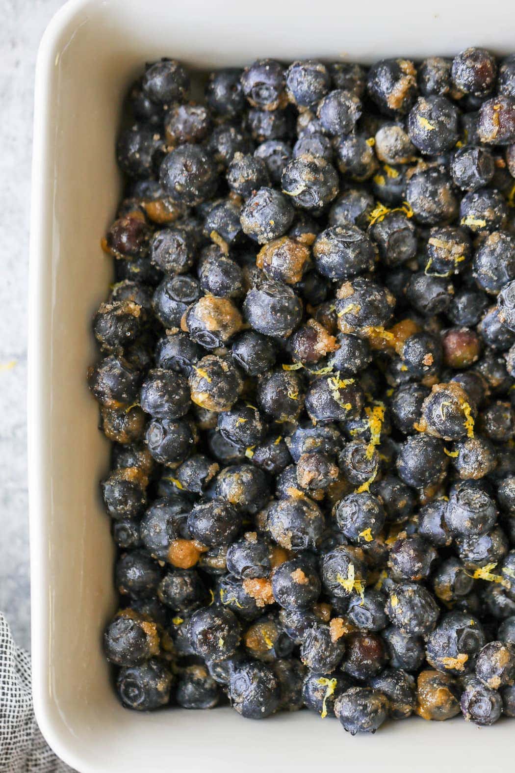 Fresh blueberries tossed in brown sugar, cinnamon, and lemon zest spread evenly in a white baking dish