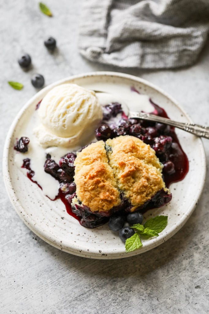 Serving of blueberry cobbler on stone plate with scoop of vanilla ice cream