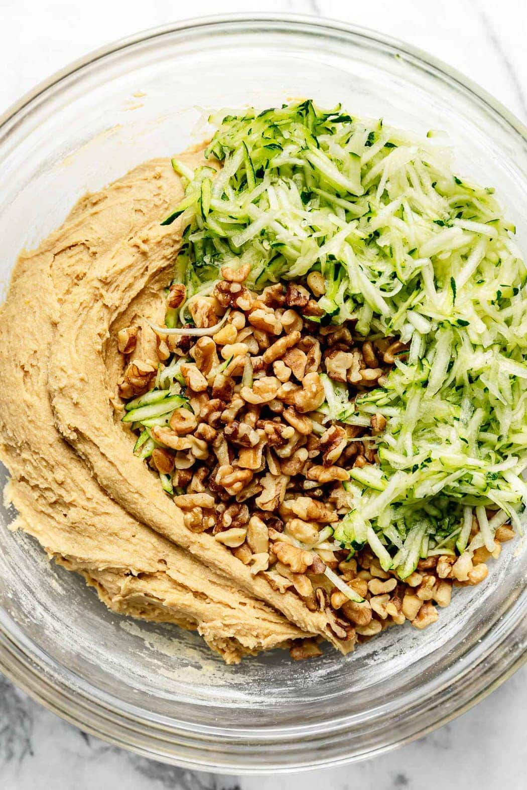 Freshly grated zucchini and chopped walnuts on top of zucchini bread batter waiting to be folded in.