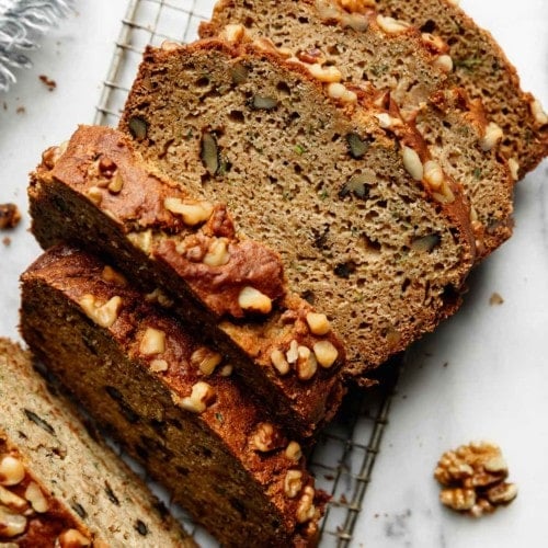 Thick slices of freshly baked zucchini bread topped with walnuts on a metal cooling rack