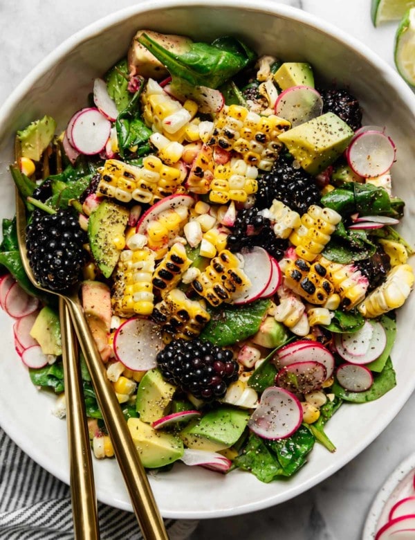 Grilled Corn Salad with blackberries and diced avocado in a white serving bowl with gold cutlery