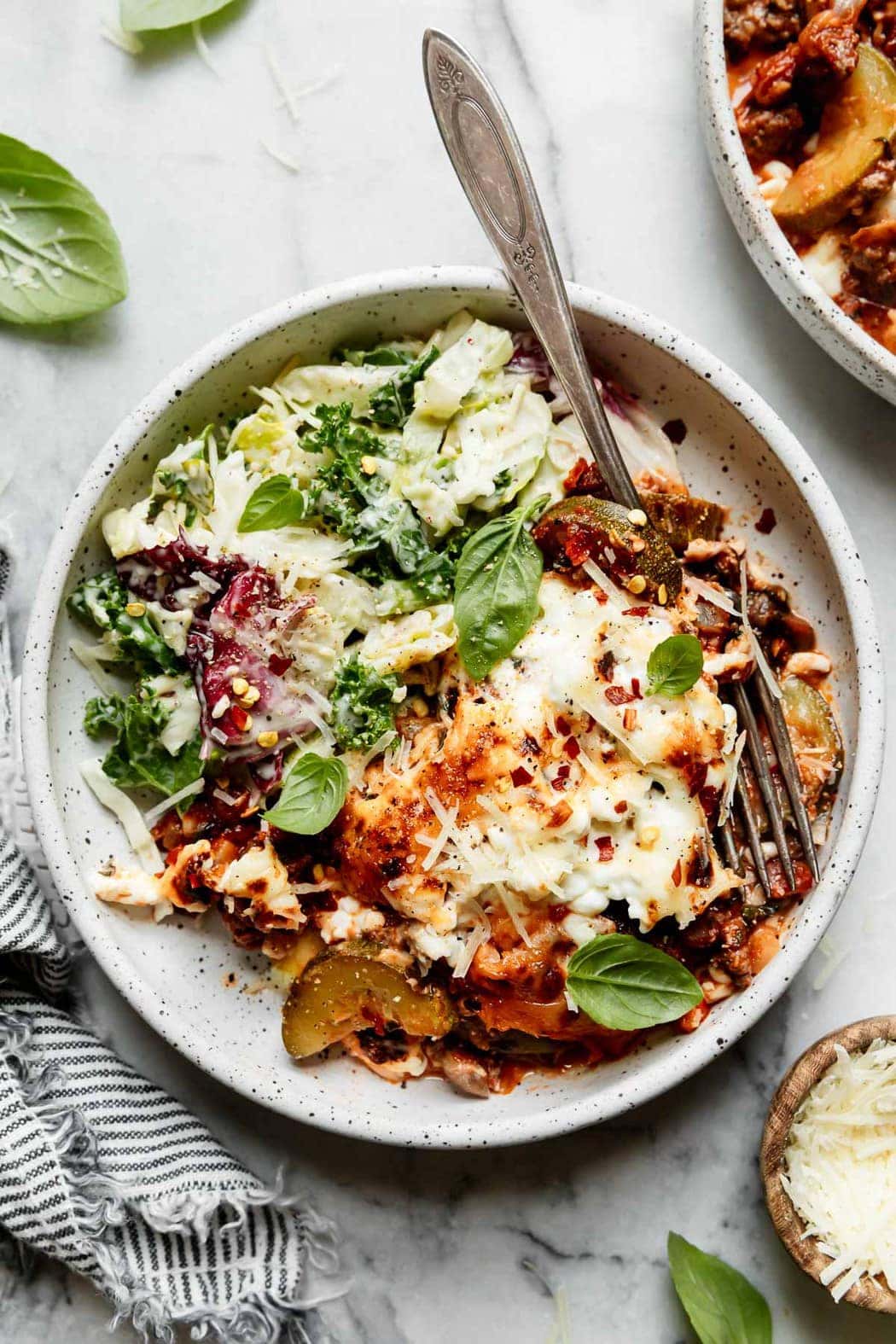 Zucchini lasagna topped with cottage cheese and mozzarella cheese plated on a speckled plate with a caesar salad on the side