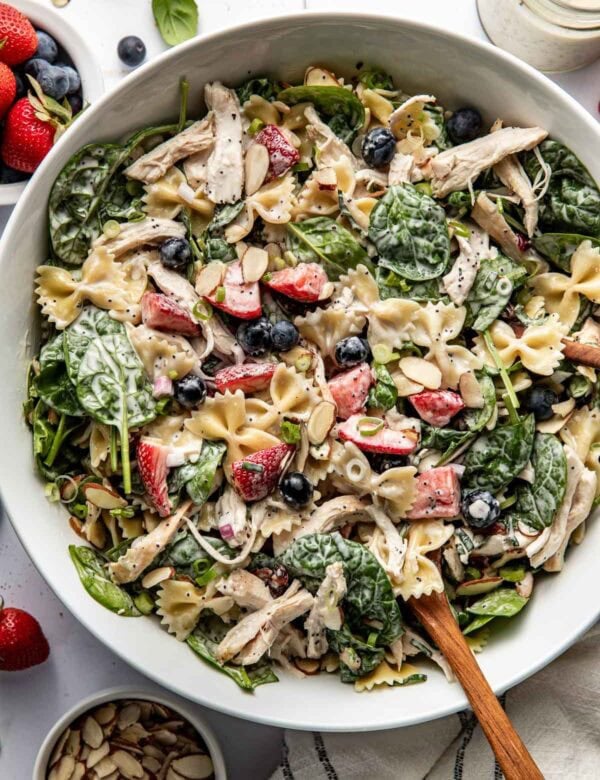 Summer pasta salad with fresh berries, shredded chicken and spinach in a large serving bowl