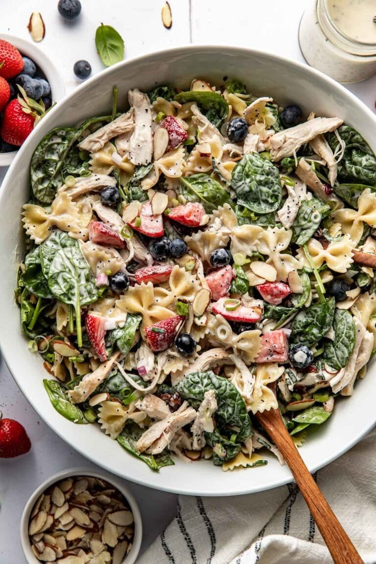 Overhead view of a large white bowl of summer berry pasta salad topped with sliced almonds.