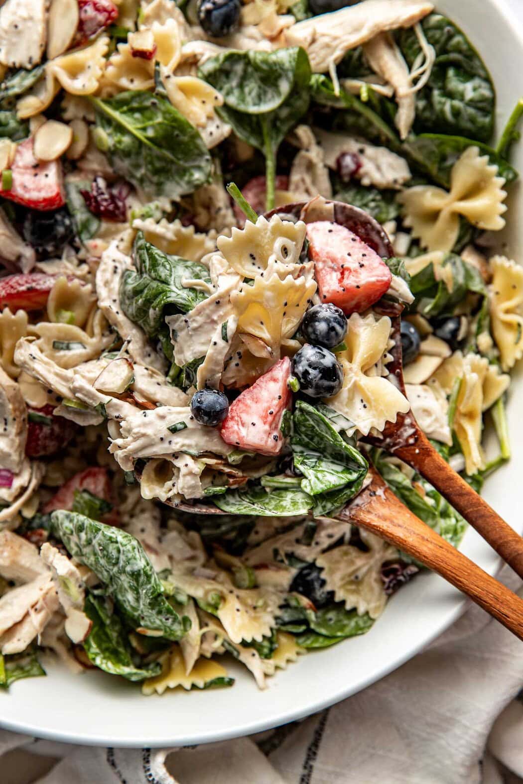 Close up view of two wooden spoons bringing up a scoop of Summer Berry Pasta Salad With Chicken.