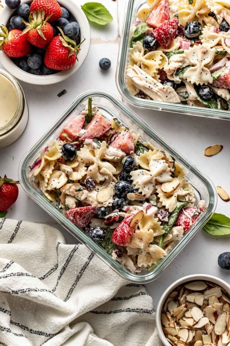 Overhead view of two glass meal prep containers filled with summer berry pasta salad topped with fresh basil.