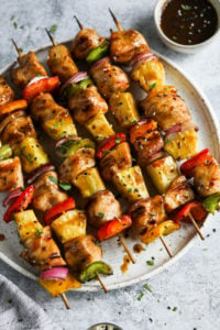 Grilled chicken kebabs with pineapple and colored peppers on skewers plated on a round plate