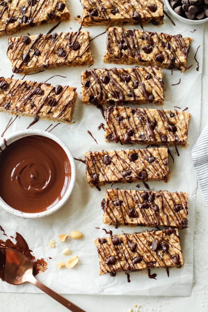 Several vegan protein bars laying in a scattered line on parchment paper freshly drizzled with chocolate