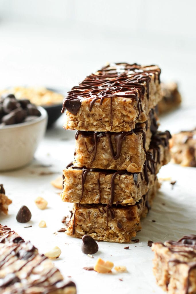 Four homemade peanut butter protein bars with chocolate chips stacked up with a chocolate drizzle over the tops