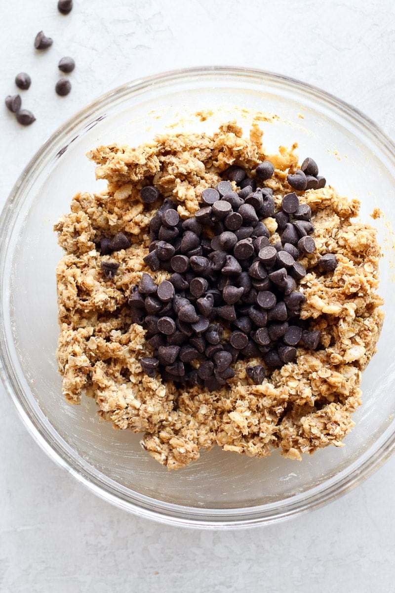 Homemade protein bar mixture in a mixing bowl with chocolate chips on top ready to be folded in