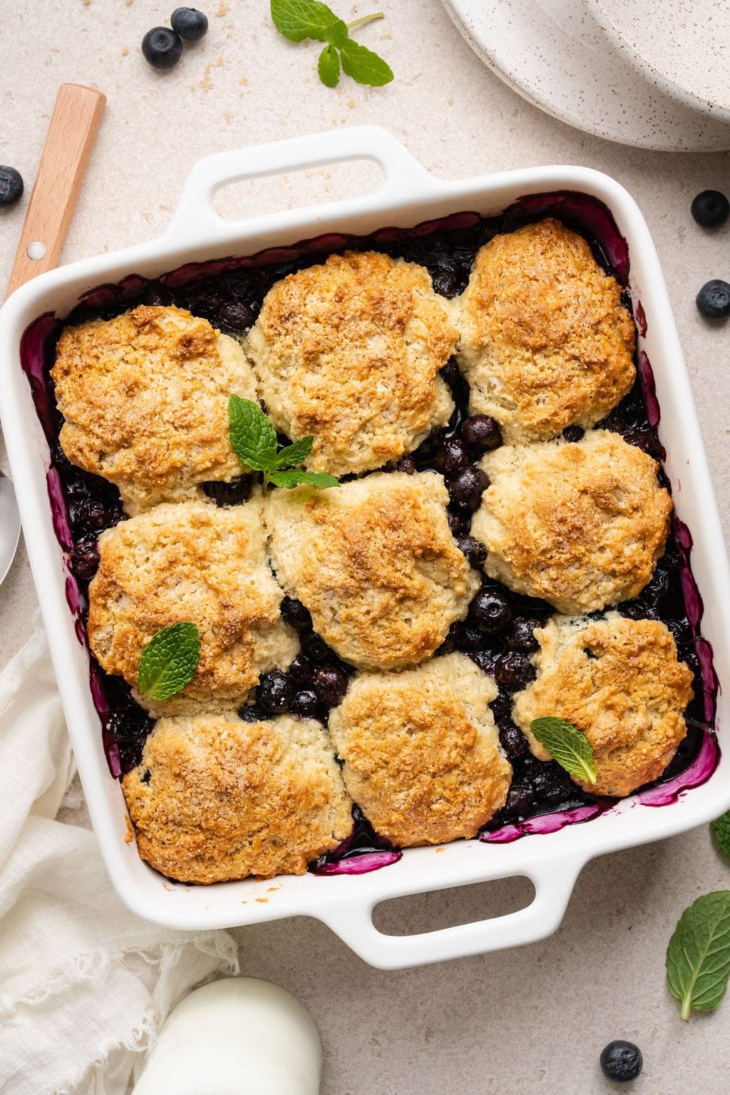 Overhead view of a square white baking dish filled with freshly baked Blueberry Cobbler topped with fresh mint leaves
