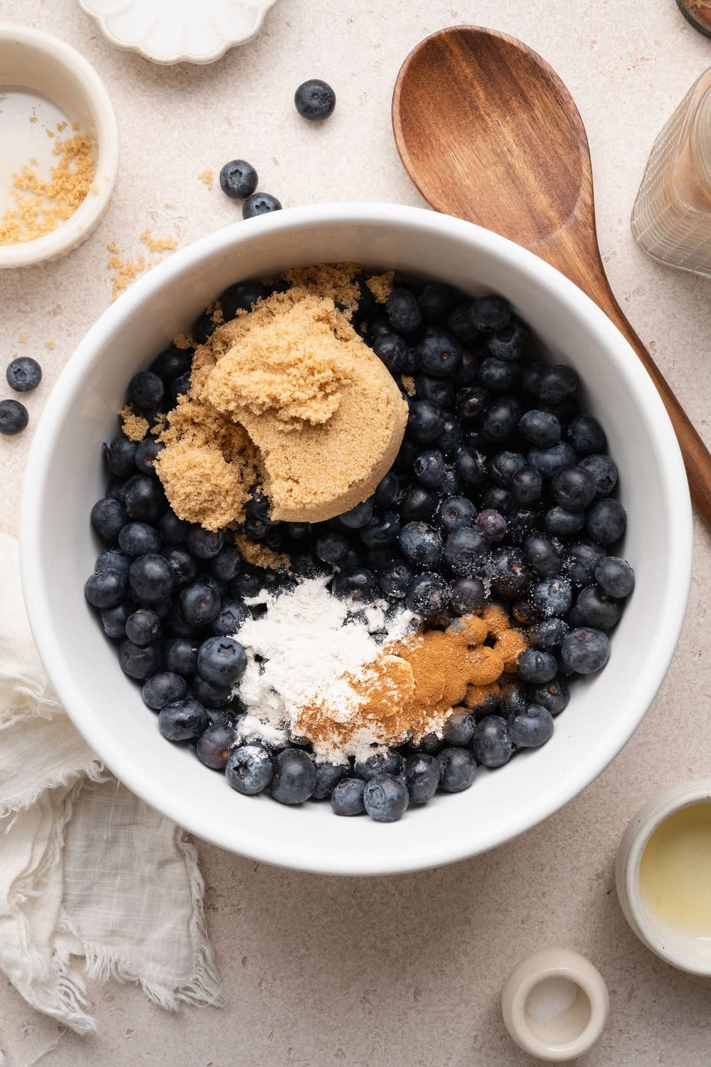Overhead view of a bowl of blueberries, brown sugar, cinnamon and spices ready for stirring.