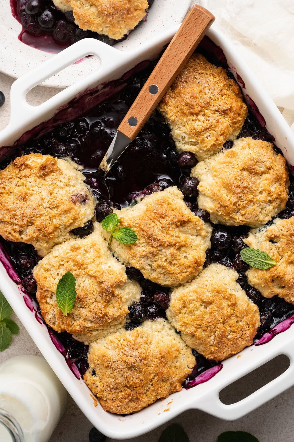 Overhead view of a baking dish filled with Blueberry Cobbler garnished with fresh mint leaves.