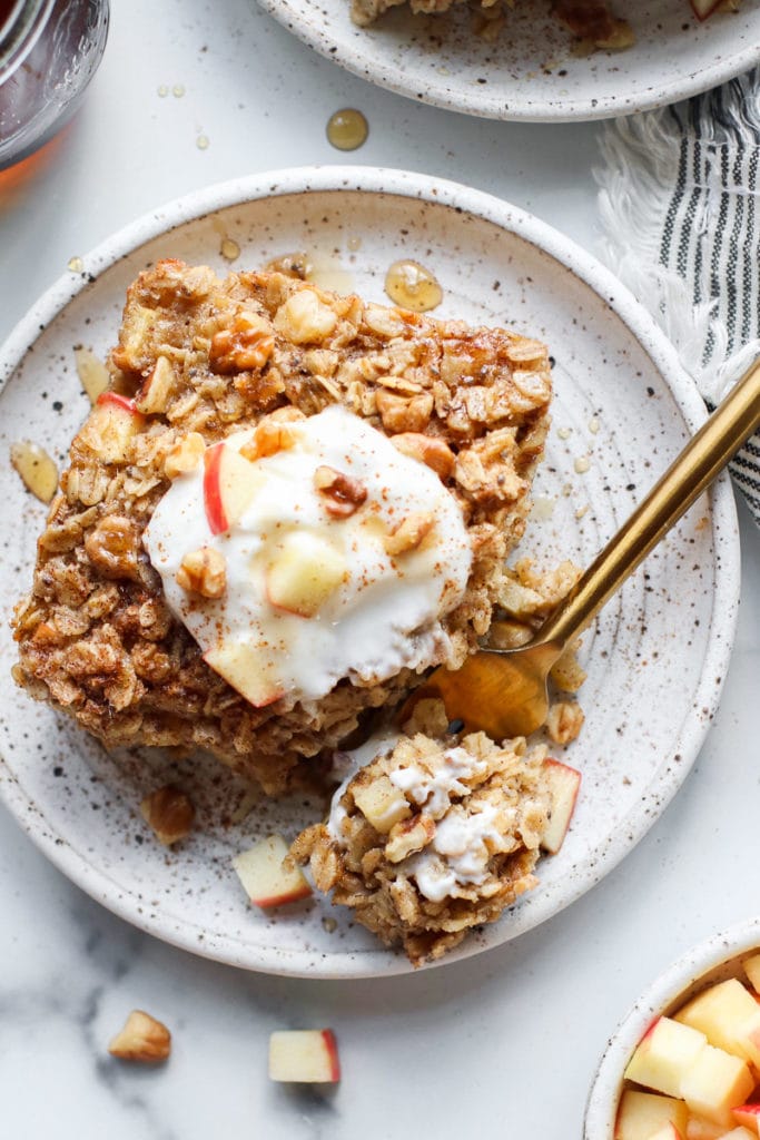 Overhead view of apple cinnamon baked oatmeal topped with yogurt and maple syrup drizzles on a speckled plate