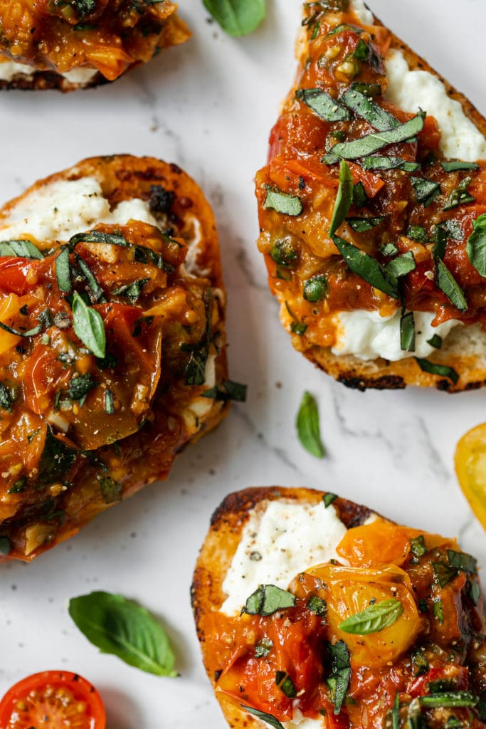 Close up of burrata topped bruschetta with juicy sautéed tomatoes and fresh basil