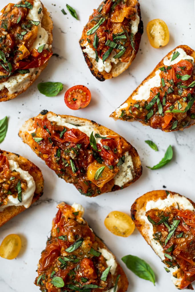 Several slices of bruschetta topped with burrata and sautéed tomatoes on a countertop