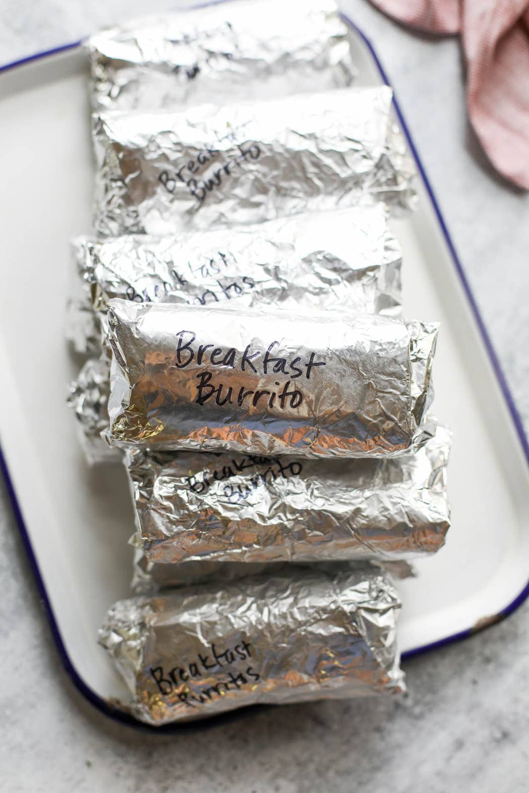 A stack of breakfast burritos on a white metal tray ready for placing in the freezer
