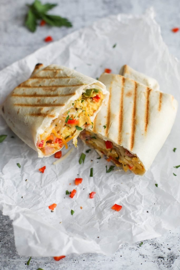 An omelet and ham filled freezer breakfast burrito cut in half with grill marks on the tortilla