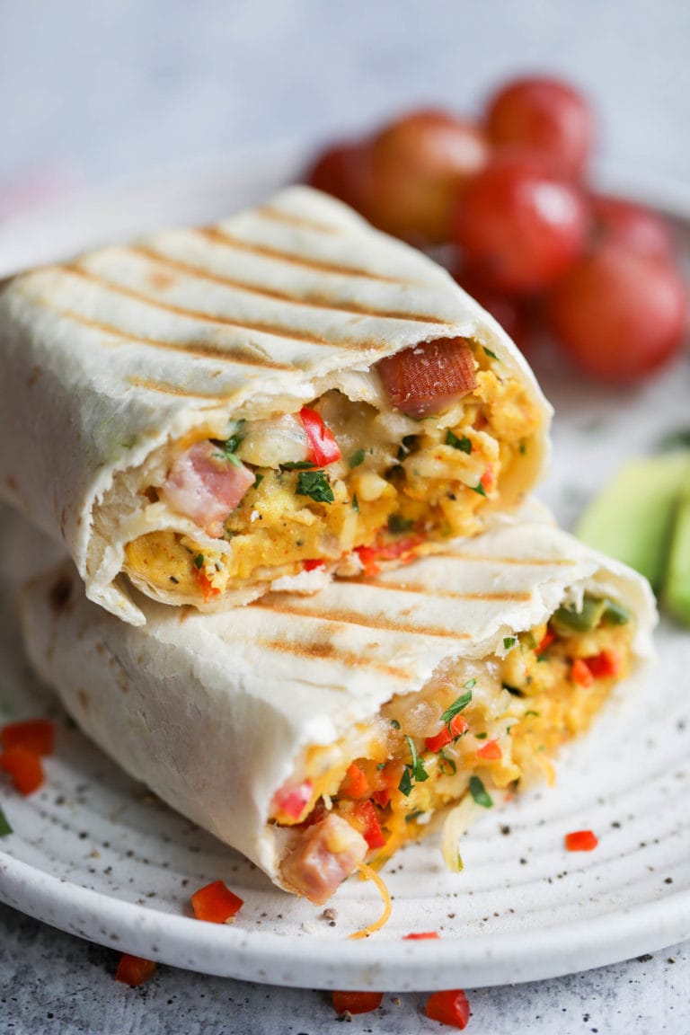 A breakfast burrito filled with scrambled eggs and ham cut in half with grill marks on the tortilla.