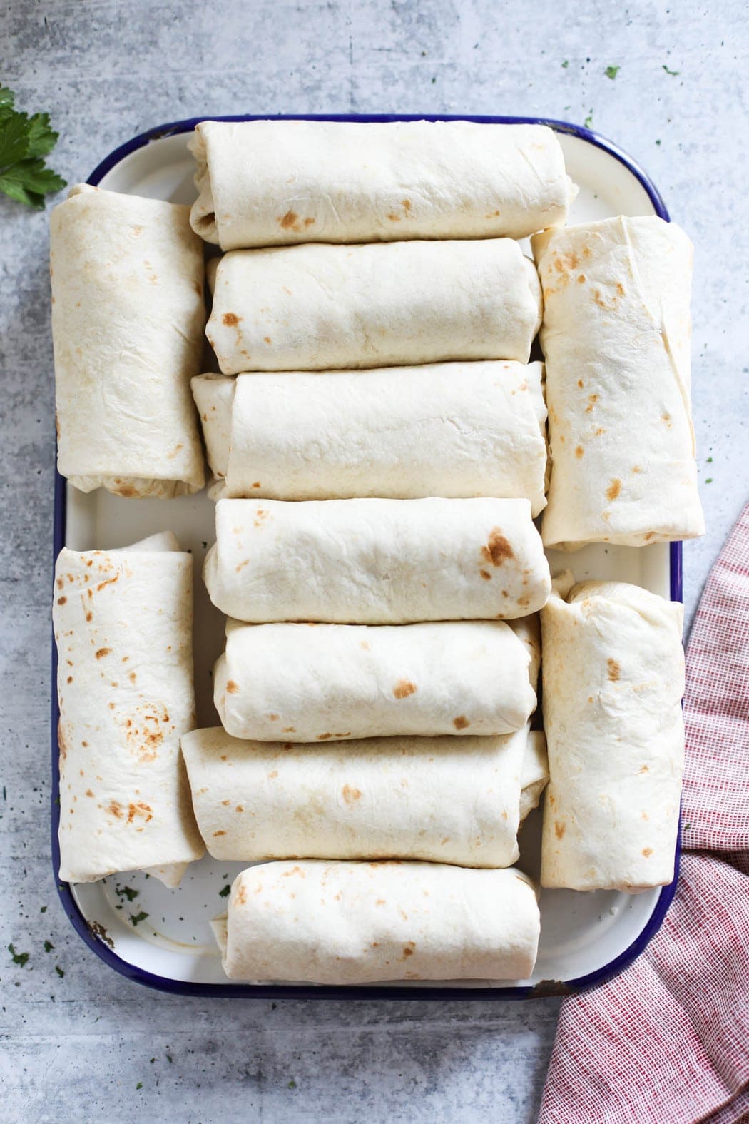 A white serving tray filled with rolled breakfast burritos ready for the freezer