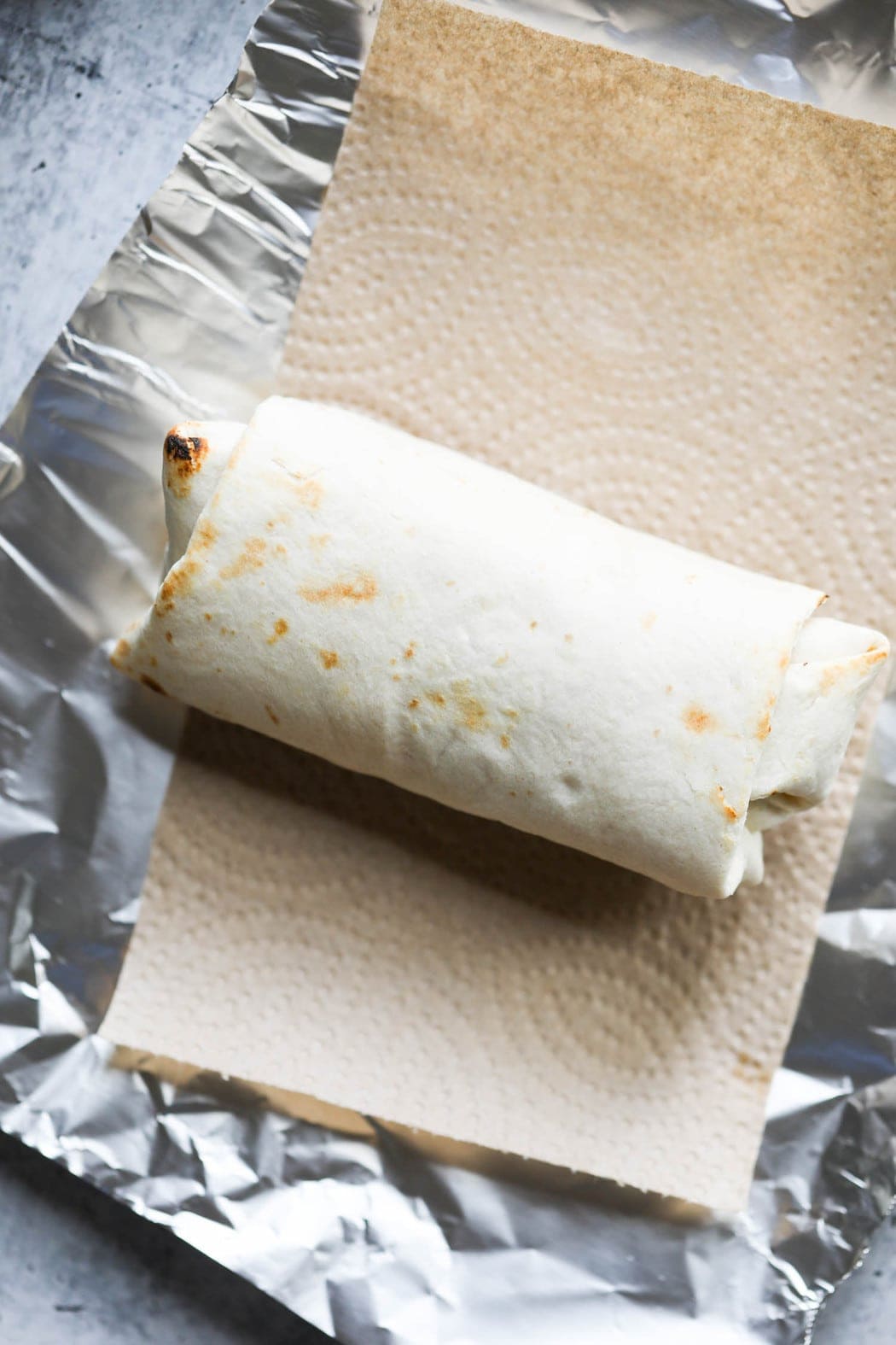 A breakfast burrito rolled up placed on a paper towel and piece of foil